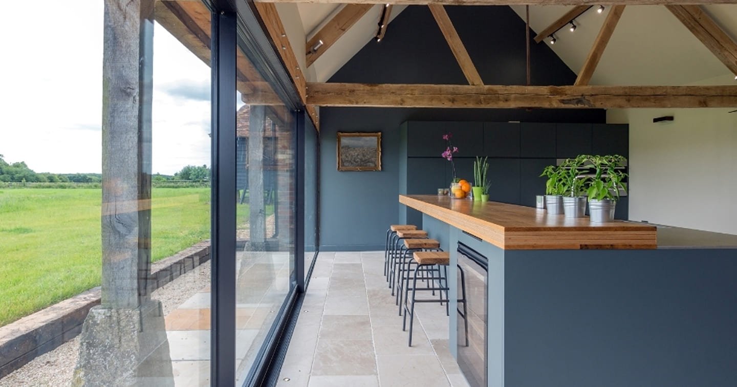 Barn-style home extension Kilsyth - exposed timber roof trusses, full-height sliding glass doors, natural stone floor and kitchen island