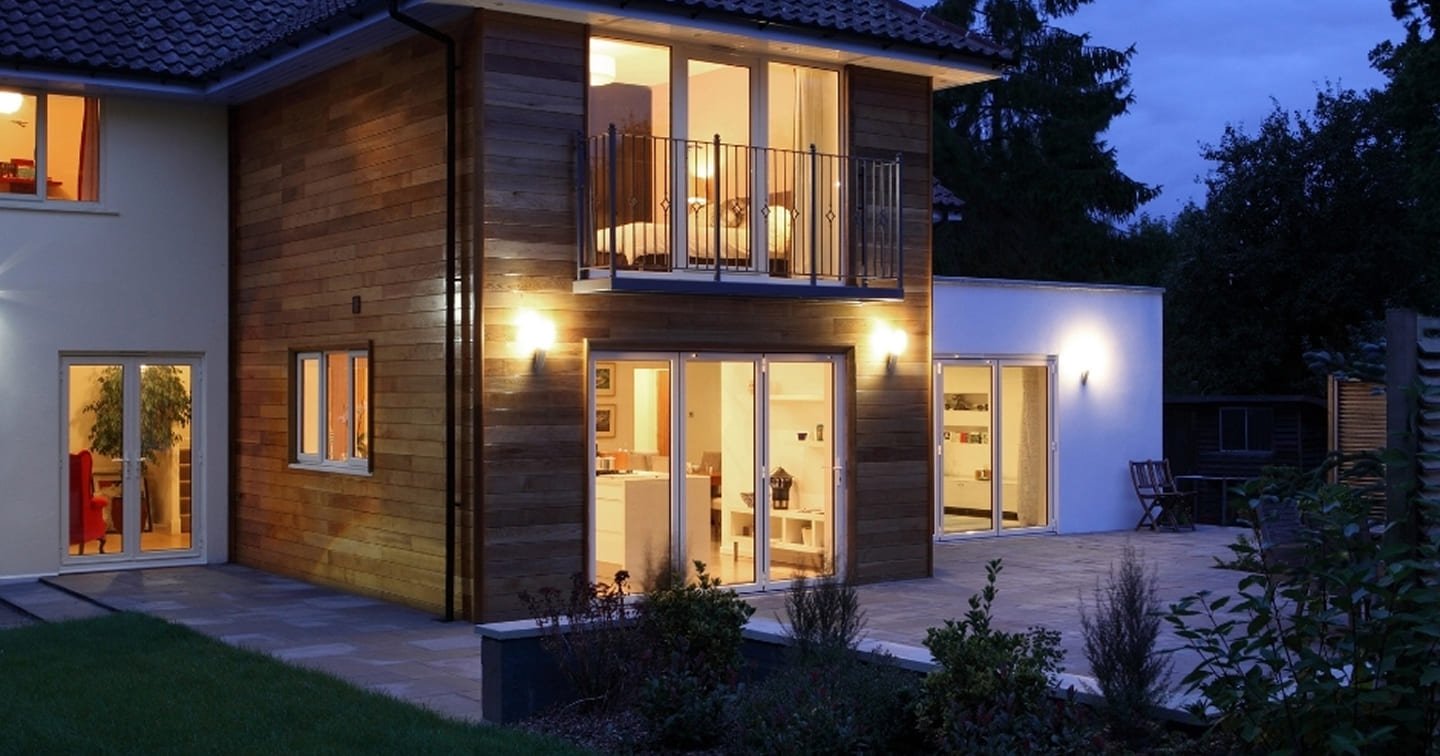 Two-storey home extension Knoxfield at dusk - timber cladding on upper level, full-height glazing, balcony and landscape lighting